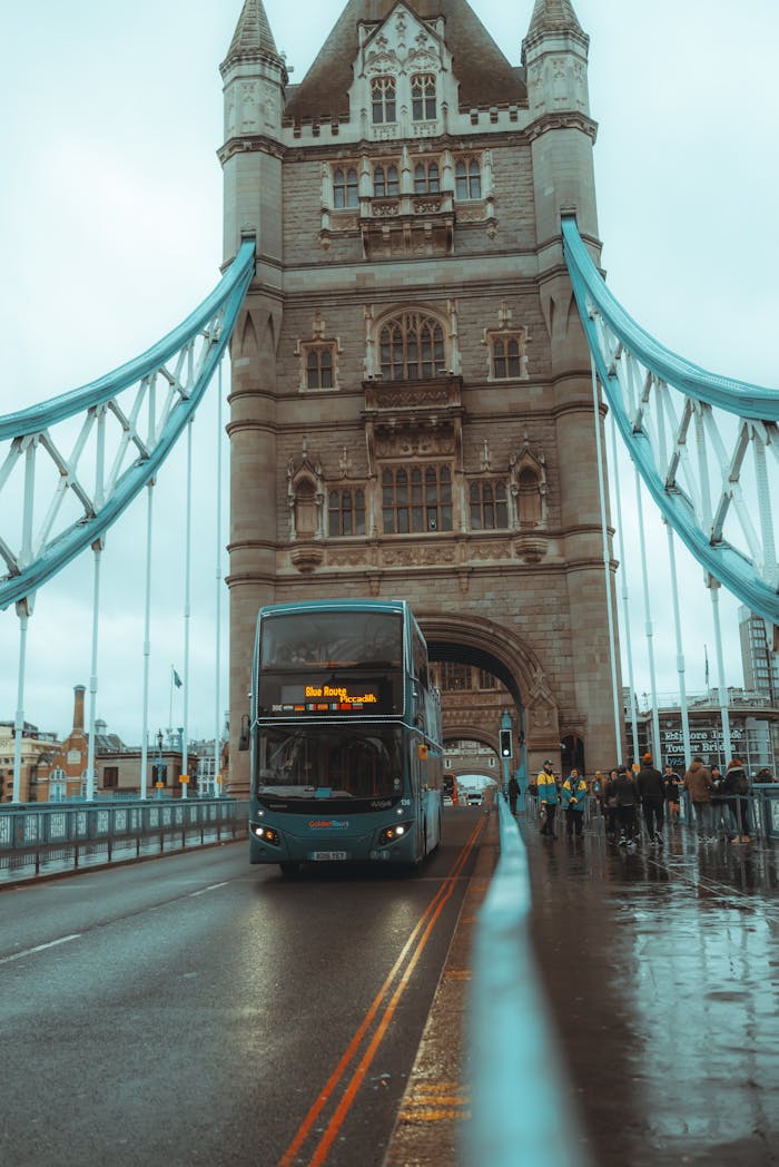 A classic London scene of a double-decker bus crossing the iconic Tower Bridge on a rainy day.